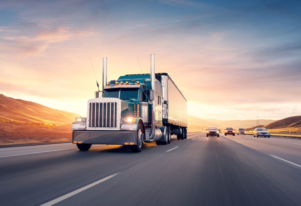 Front angle of semi truck driving down highway with sunsetting in background.