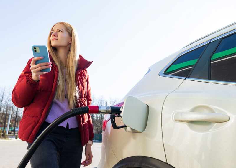 Young driver fills up car at gas station while using loyalty app on phone