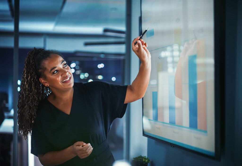 Woman presenting performance report data on large screen for stakeholders.